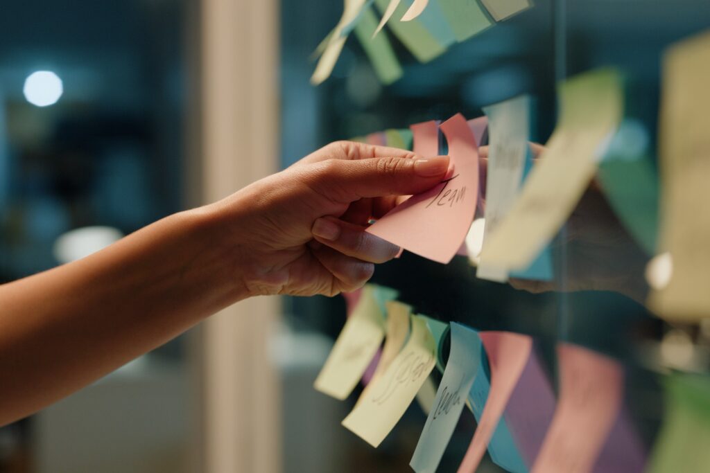 Das Foto zeigt eine Hand, die Sticky Notes an eine Scheibe anbringt. Auf der Notiz steht "Team",